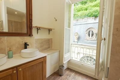 Canapé en velours brun devant une grande fenêtre lumineuse, entouré de rideaux beiges et de meubles en bois.