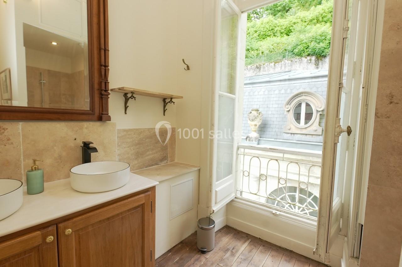 Salle de bain lumineuse avec double vasque, miroir en bois, et fenêtre ouverte sur une vue extérieure verdoyante.