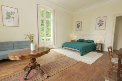 Canapé en velours brun devant une grande fenêtre lumineuse, entouré de rideaux beiges et de meubles en bois.