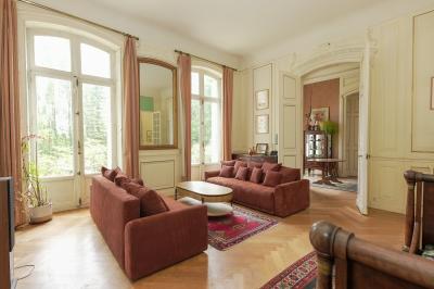 Canapé en velours brun devant une grande fenêtre lumineuse, entouré de rideaux beiges et de meubles en bois.