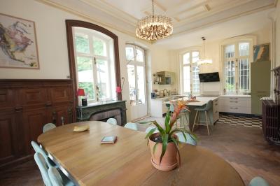 Canapé en velours brun devant une grande fenêtre lumineuse, entouré de rideaux beiges et de meubles en bois.