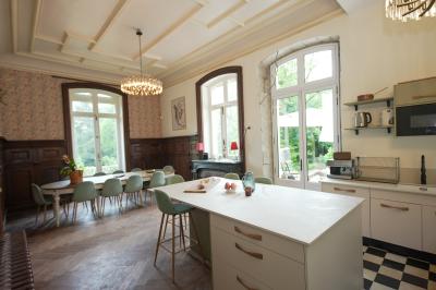 Canapé en velours brun devant une grande fenêtre lumineuse, entouré de rideaux beiges et de meubles en bois.