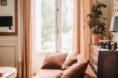 Canapé en velours brun devant une grande fenêtre lumineuse, entouré de rideaux beiges et de meubles en bois.
