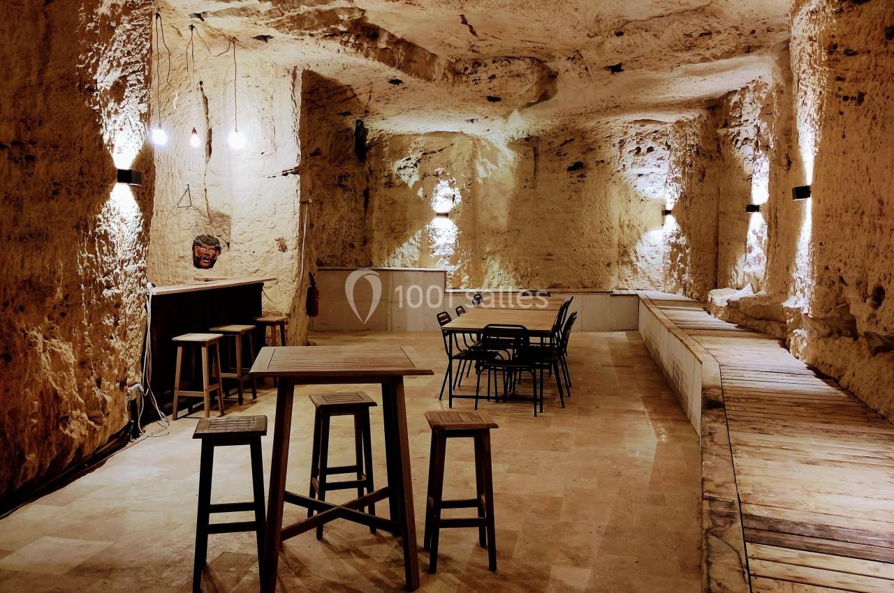 Salle souterraine en pierre avec tables, chaises et éclairage tamisé, aménagée pour des activités ou réunions.