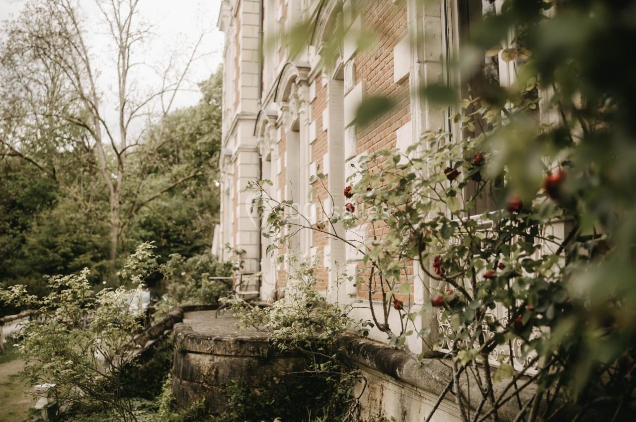 Façade d'un bâtiment ancien en briques entouré de verdure et de branches portant des pommes rouges.