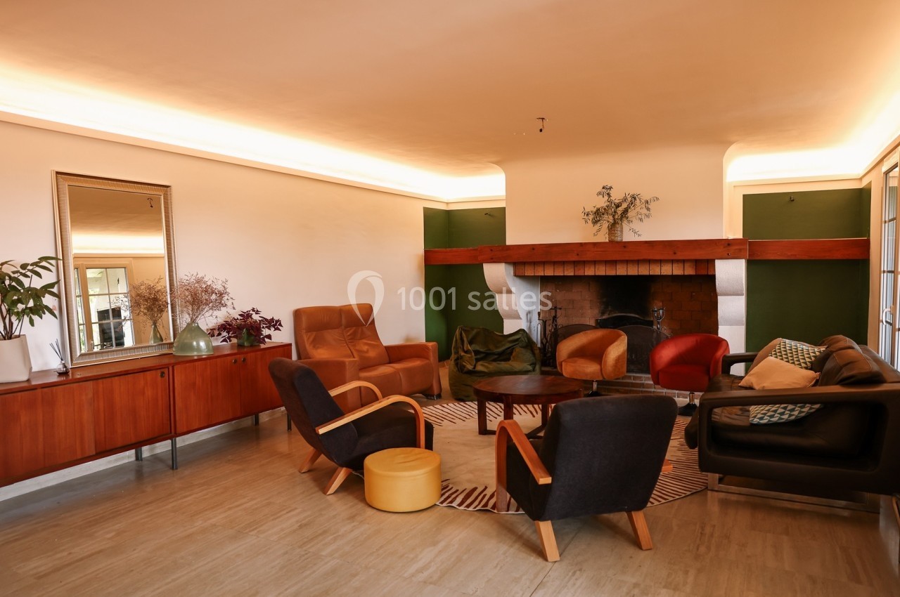 Salon chaleureux avec cheminée, mobilier vintage, fauteuils colorés, tapis rayé et buffet en bois.