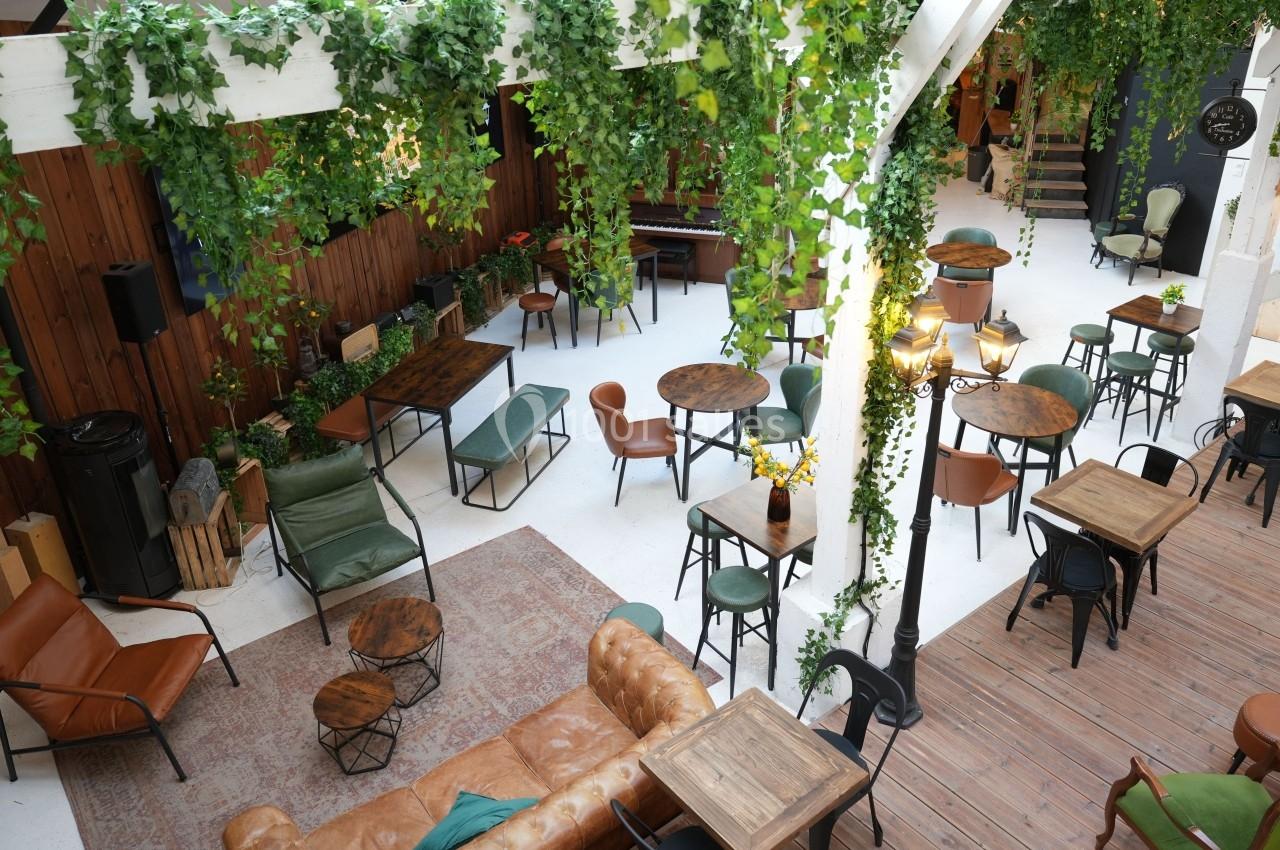 Espace intérieur lumineux avec tables, chaises et végétation suspendue, ambiance conviviale et naturelle.
