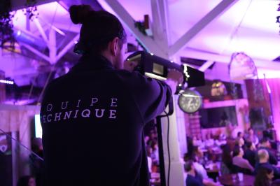 Salle comble éclairée de lumières violettes, avec un public attentif face à une scène où une personne s'exprime.