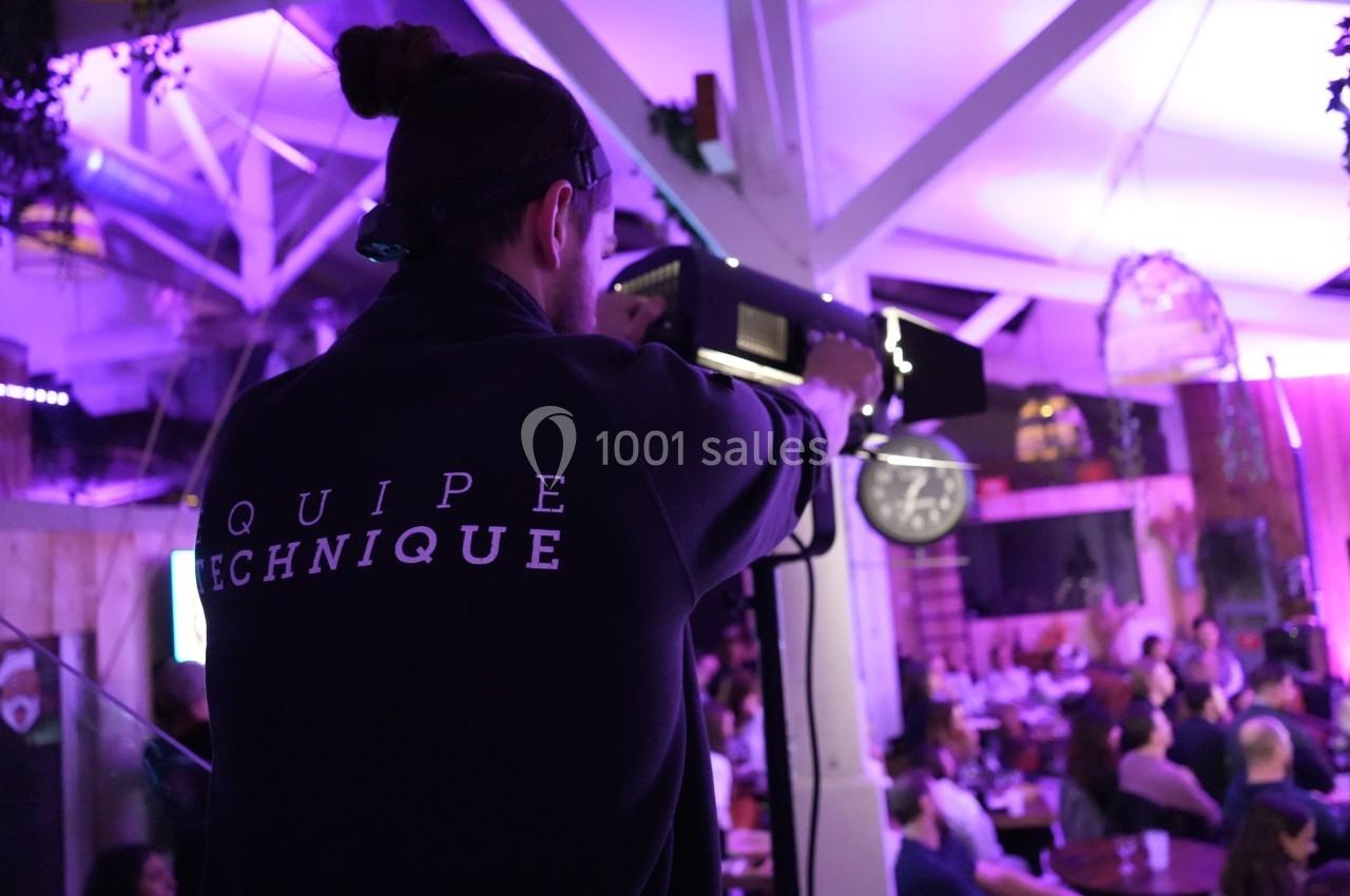 Un technicien ajuste un projecteur dans un espace intérieur éclairé, avec un public en arrière-plan.