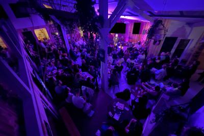 Salle comble éclairée de lumières violettes, avec un public attentif face à une scène où une personne s'exprime.