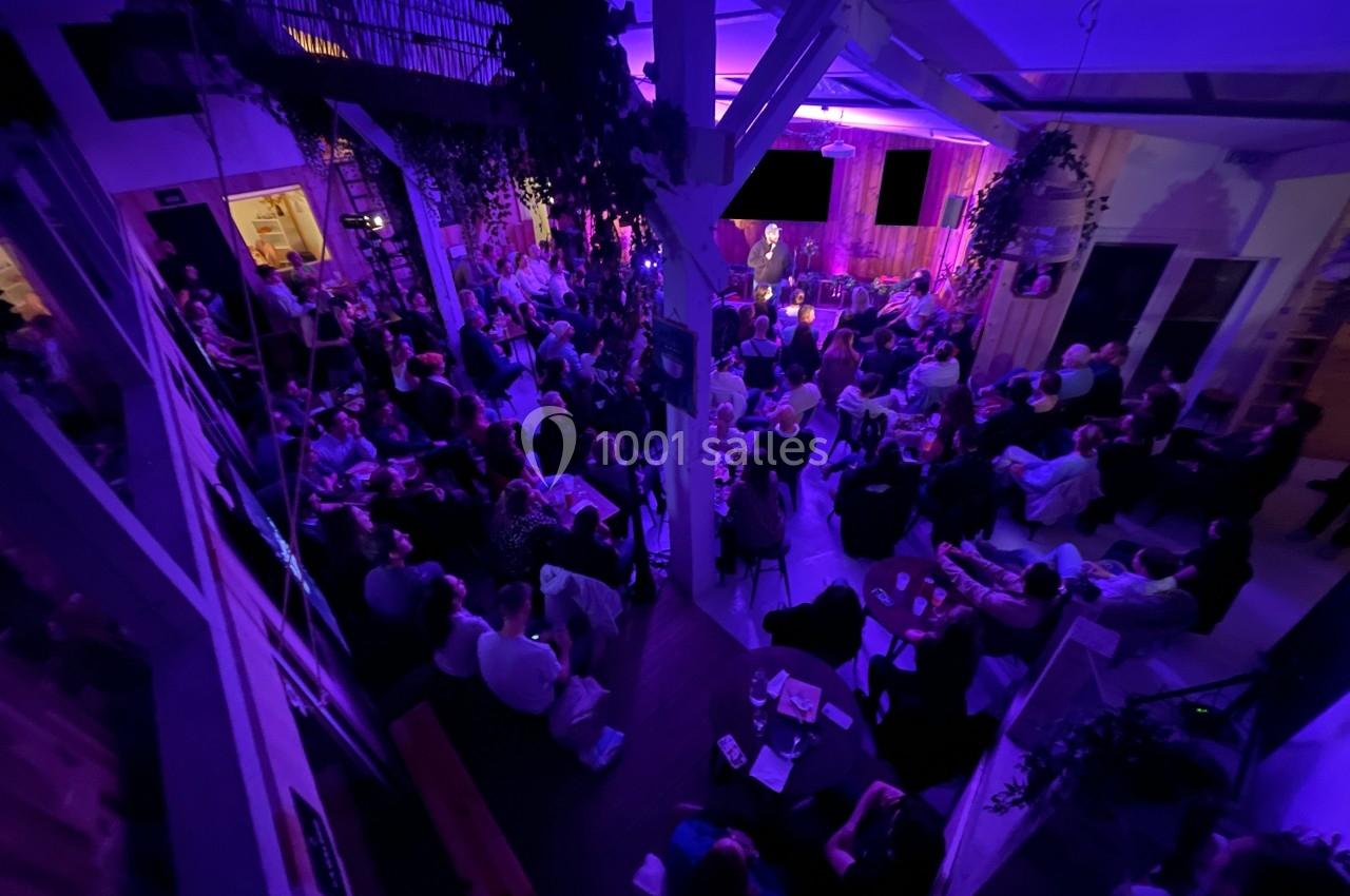 Salle comble éclairée de lumières violettes, avec un public attentif face à une scène où une personne s'exprime.