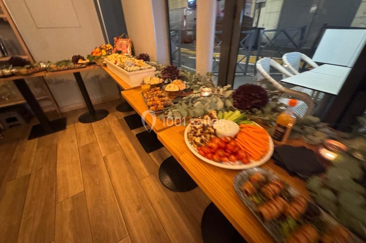 Buffet composé de légumes, fruits, brochettes et autres plats, disposé sur plusieurs tables en bois dans une salle.