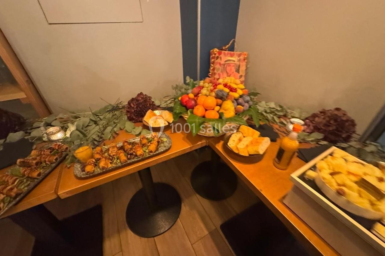 Buffet composé de brochettes, fruits, pains et jus disposés sur des tables décorées de feuillages et fleurs.