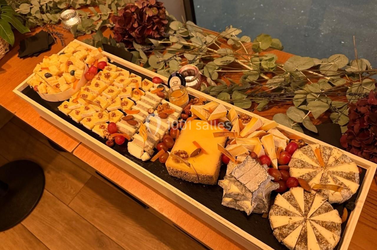Plateau de fromages variés avec fruits secs, raisins et condiments, disposé sur une table en bois décorée de feuillage.