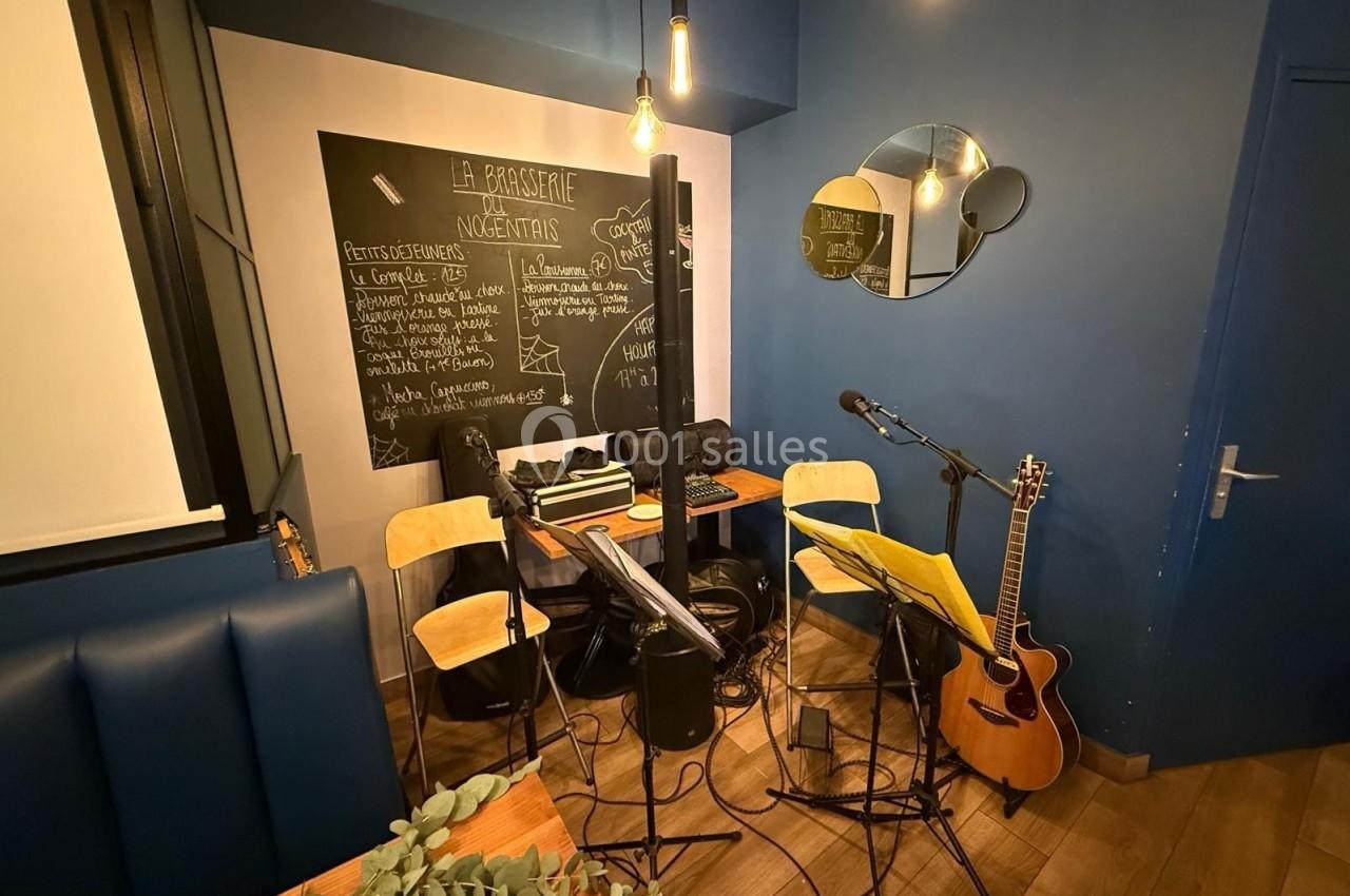 Espace de musique avec guitares, micros, pupitres et tableau noir affichant des informations dans une pièce bleue.