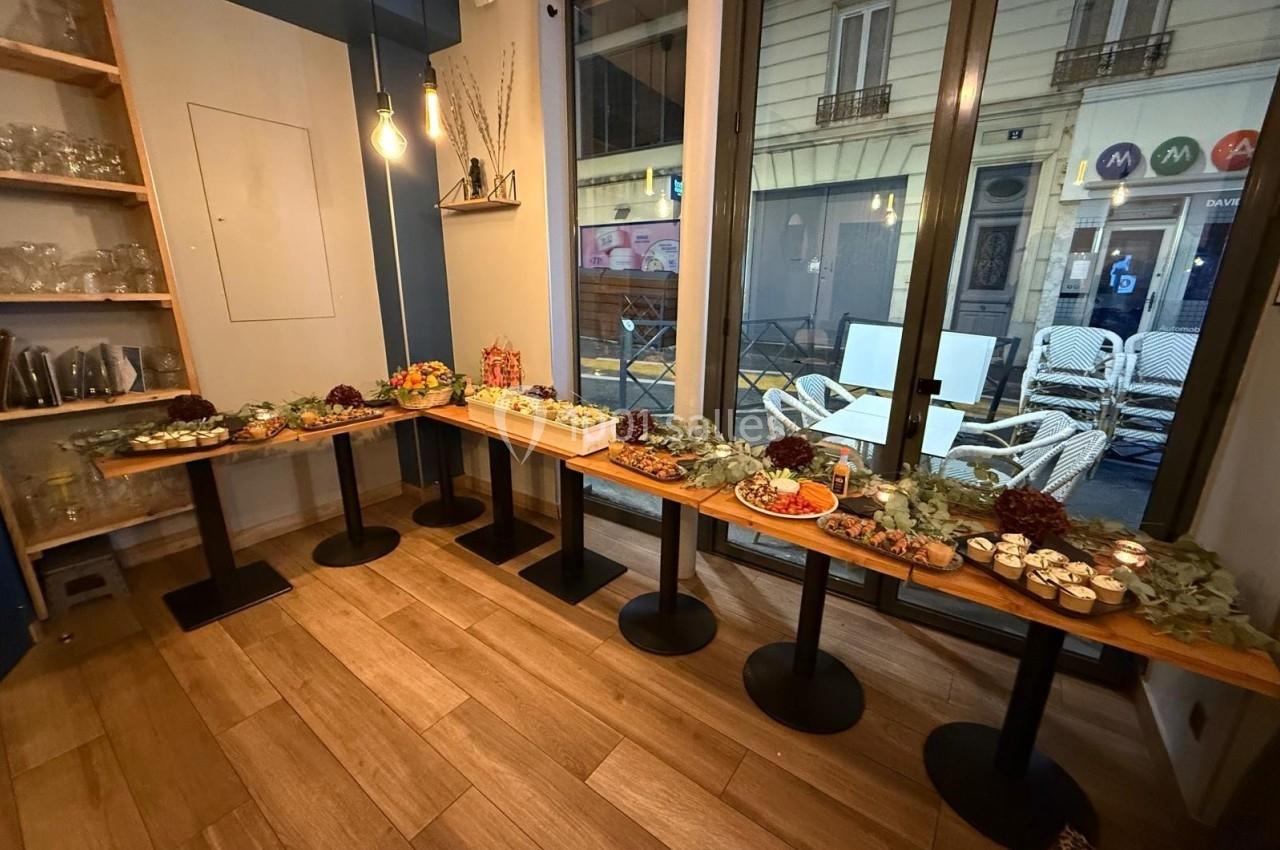Buffet disposé sur des tables en bois, avec divers plats et décorations, dans une salle lumineuse avec vue sur la rue.