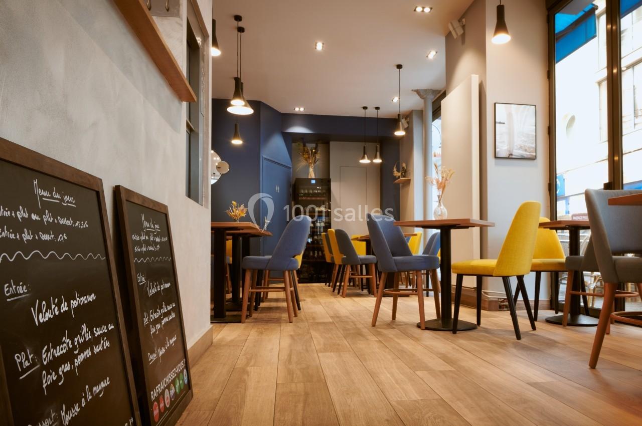 Salle de restaurant moderne avec tables en bois, chaises colorées et menus écrits à la craie sur des ardoises.