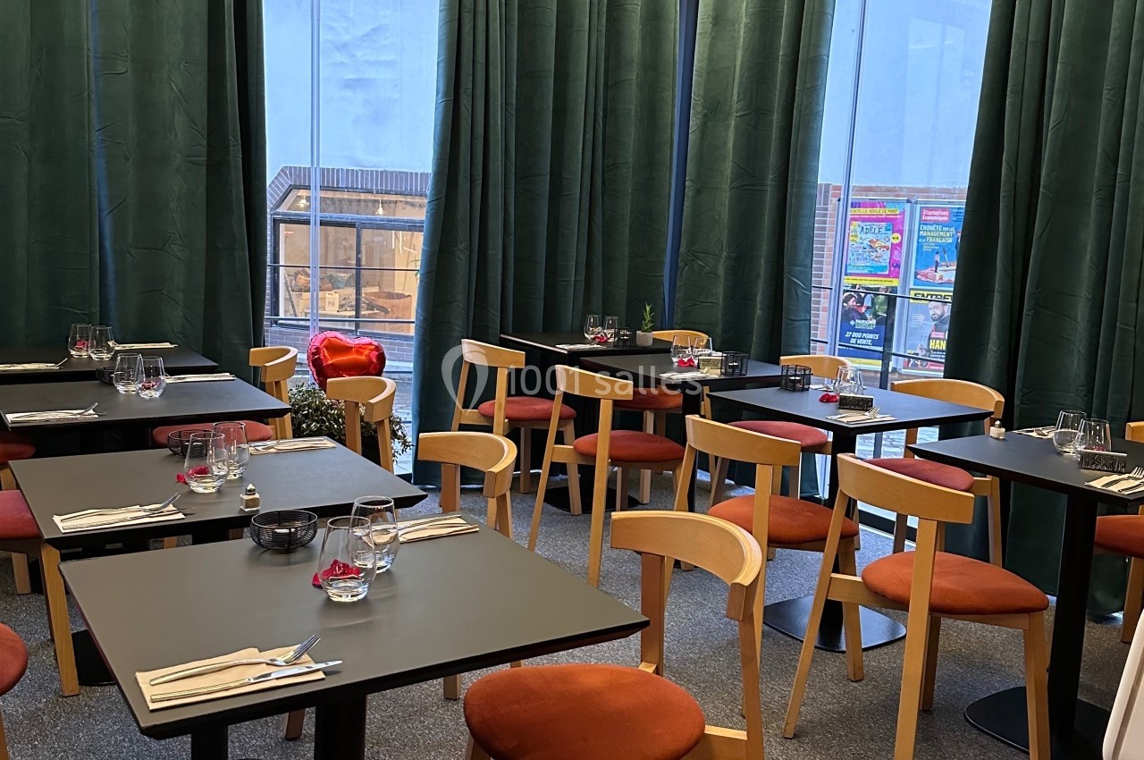 Salle de restaurant moderne avec tables dressées, chaises en bois et grandes baies vitrées donnant sur l'extérieur.
