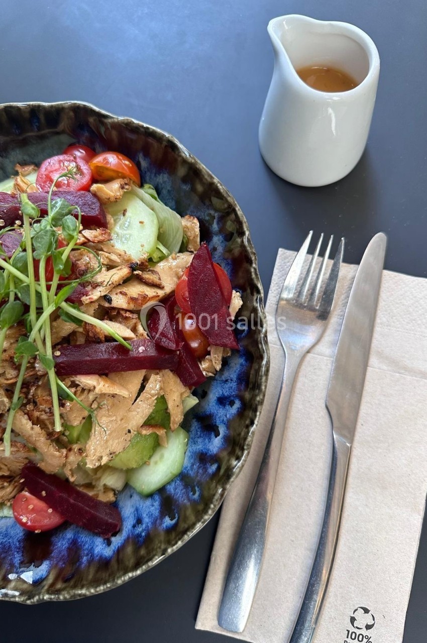 Salade composée de légumes frais, poulet effiloché et betteraves, avec une vinaigrette à part et des couverts sur une…