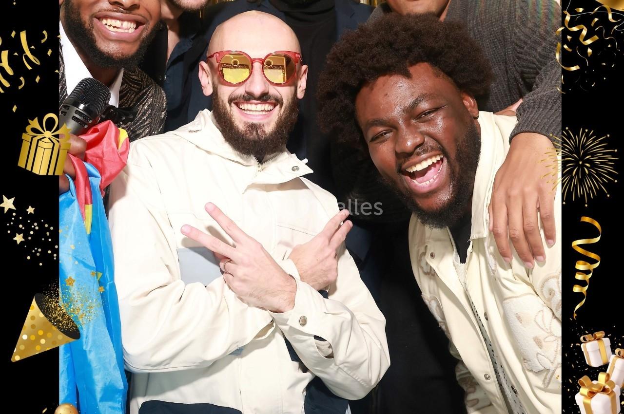 Un groupe d'hommes souriants posant devant un rideau doré lors d'une fête d'anniversaire.