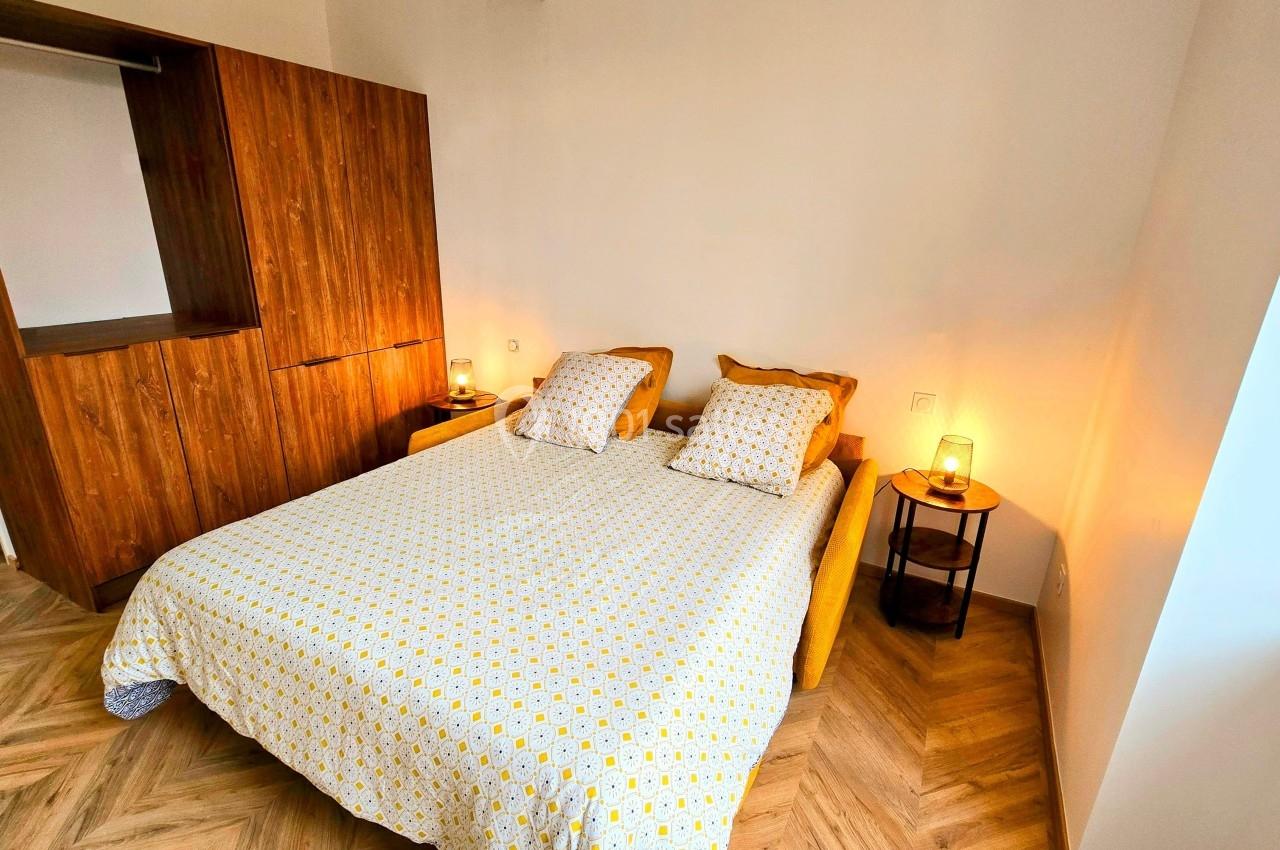 Chambre lumineuse avec un lit double, une armoire en bois, des tables de chevet et un sol en parquet.