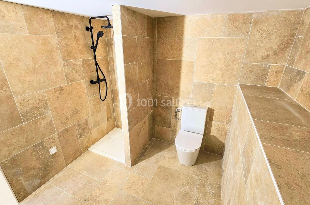 Salle de bain avec carrelage beige, douche à l'italienne avec robinetterie noire et toilettes modernes.