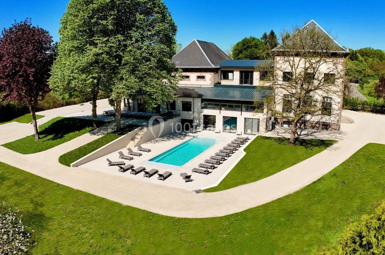 Vue aérienne d'une grande maison entourée de verdure avec une piscine et des chaises longues disposées autour.