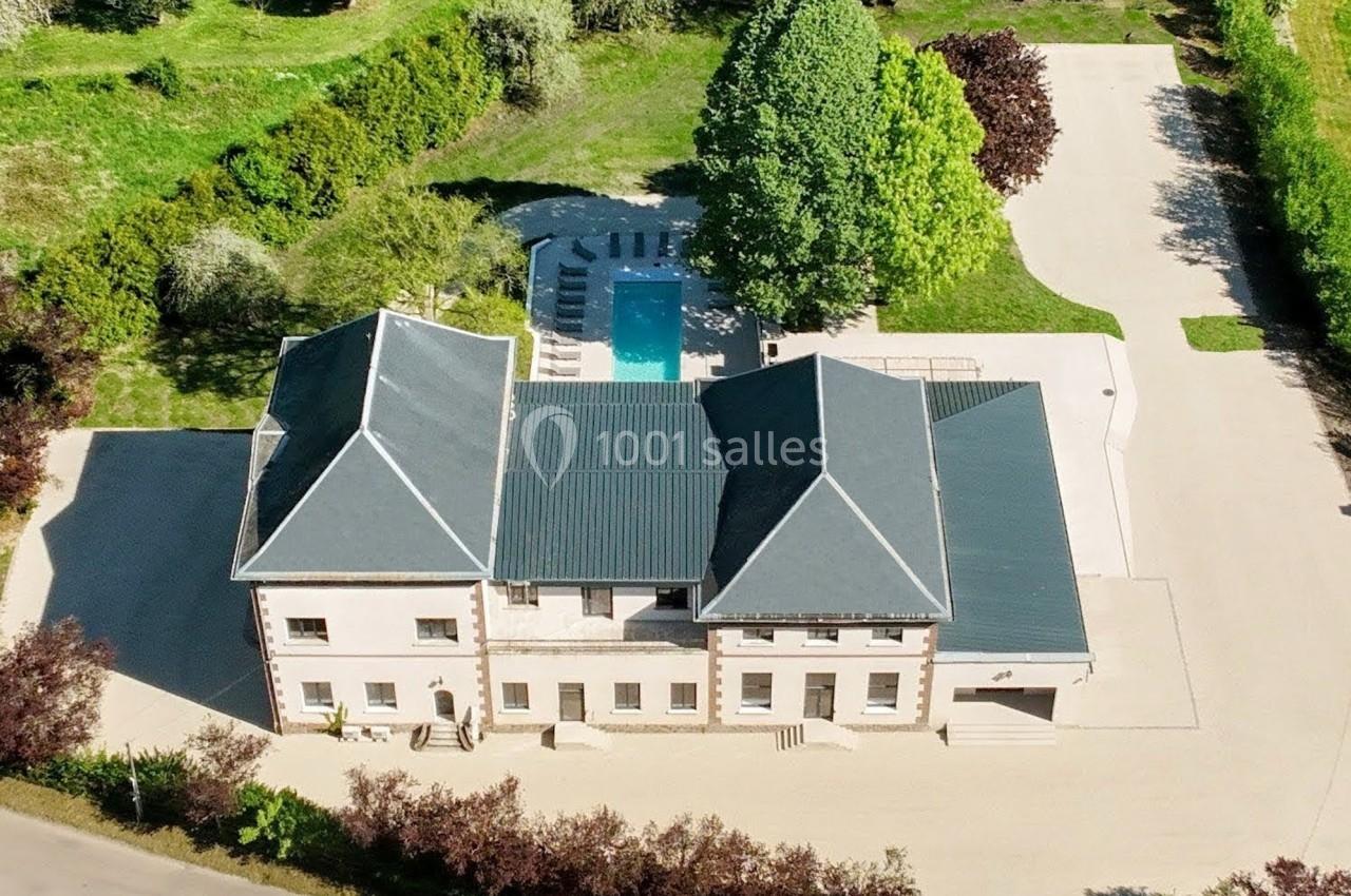 Vue aérienne d'une grande maison entourée de jardins, avec une piscine et une allée pavée.