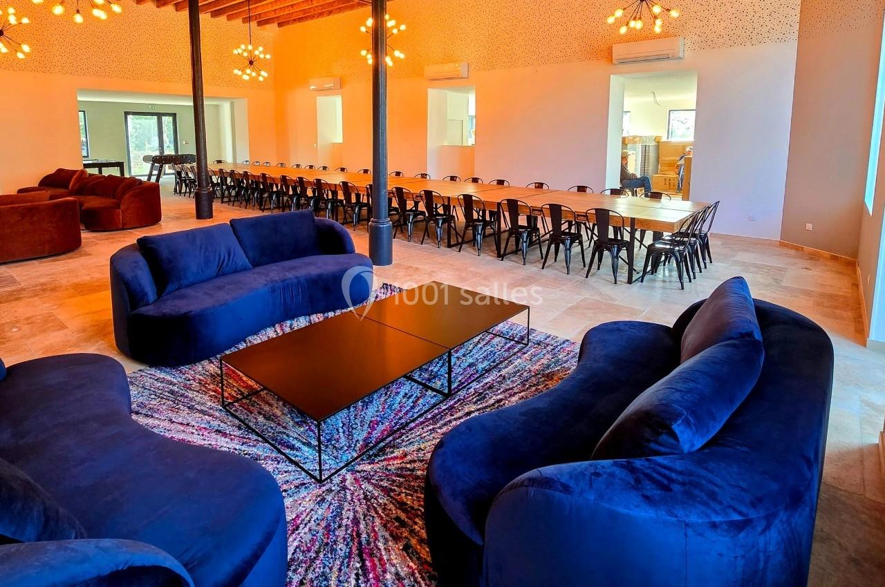 Salle spacieuse avec canapés bleus autour d'une table basse, grande table à manger en arrière-plan.