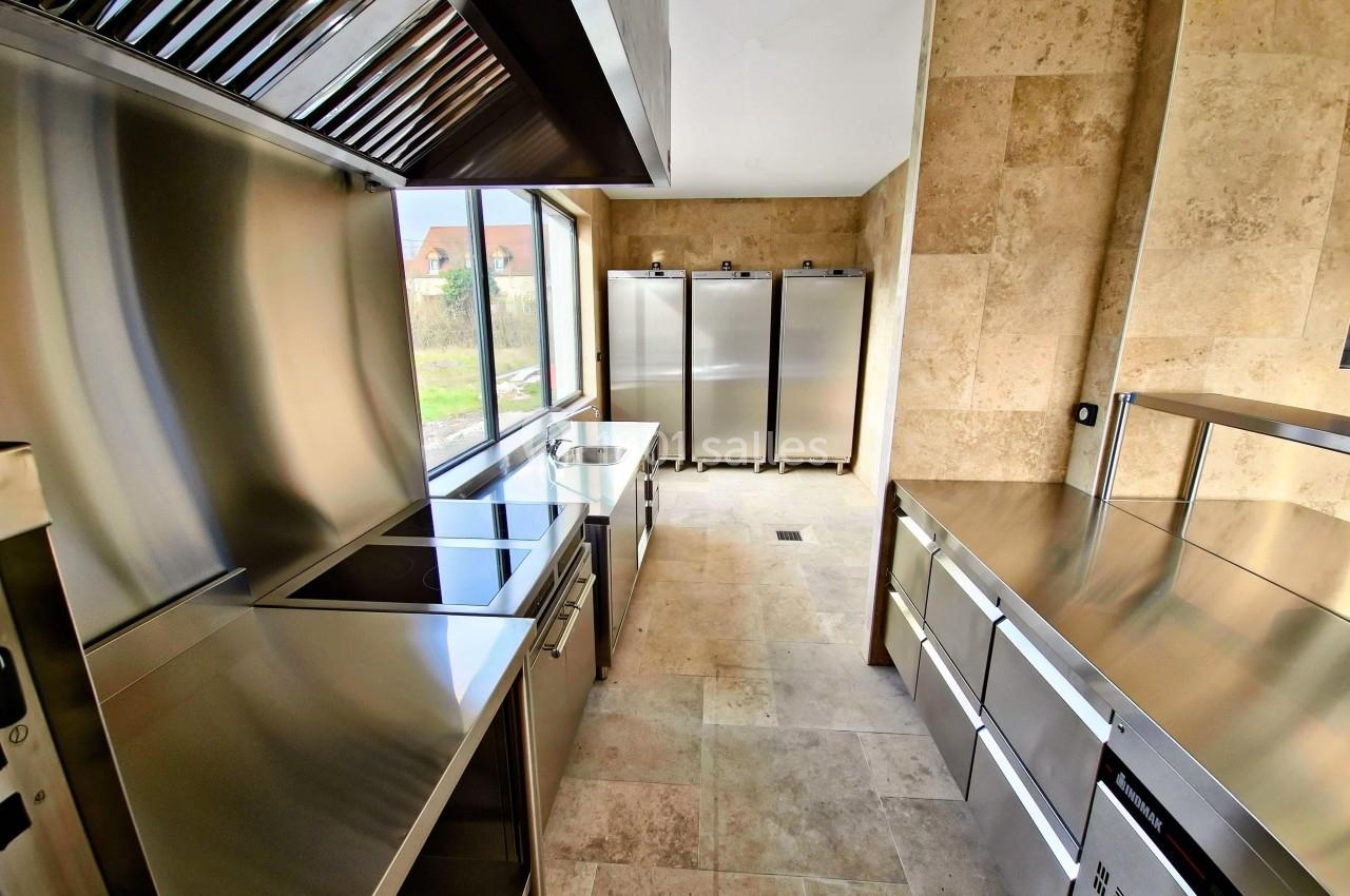 Cuisine professionnelle moderne avec équipements en acier inoxydable, plan de travail et réfrigérateurs alignés.