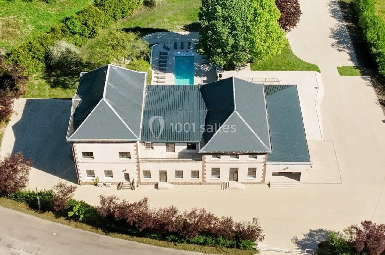 Vue aérienne d'une grande maison avec toit en ardoise, piscine extérieure et allée bordée de verdure.
