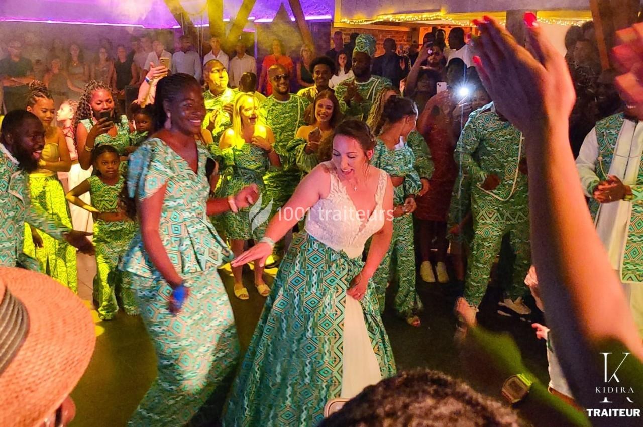 Des invités dansent lors d'une fête, avec une mariée en robe blanche entourée de personnes en tenues traditionnelles…