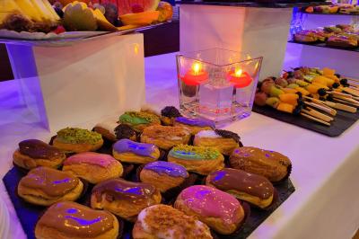 Plateau d'éclairs colorés, fruits frais et bougies décoratives sur une table de buffet.