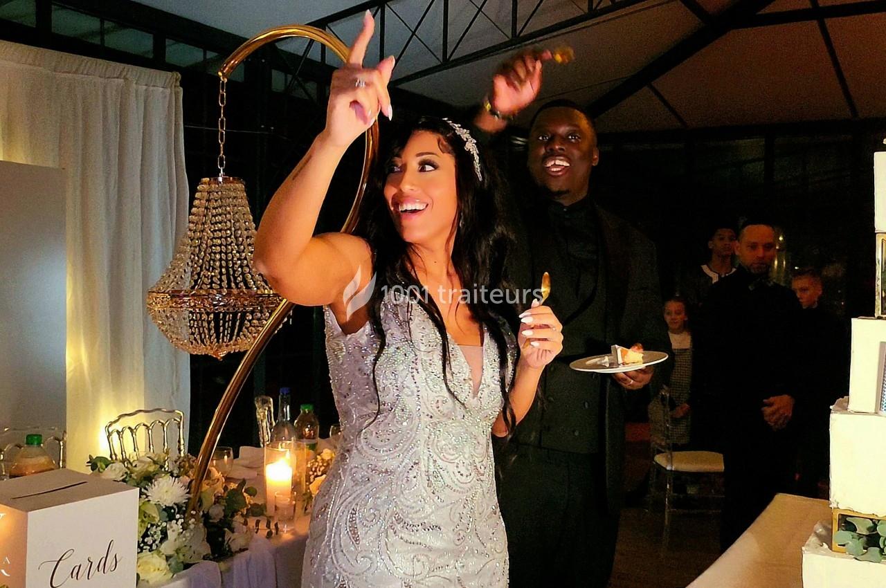 Une mariée souriante pointe du doigt tandis qu'un homme en costume tient une assiette lors d'une réception de mariage.