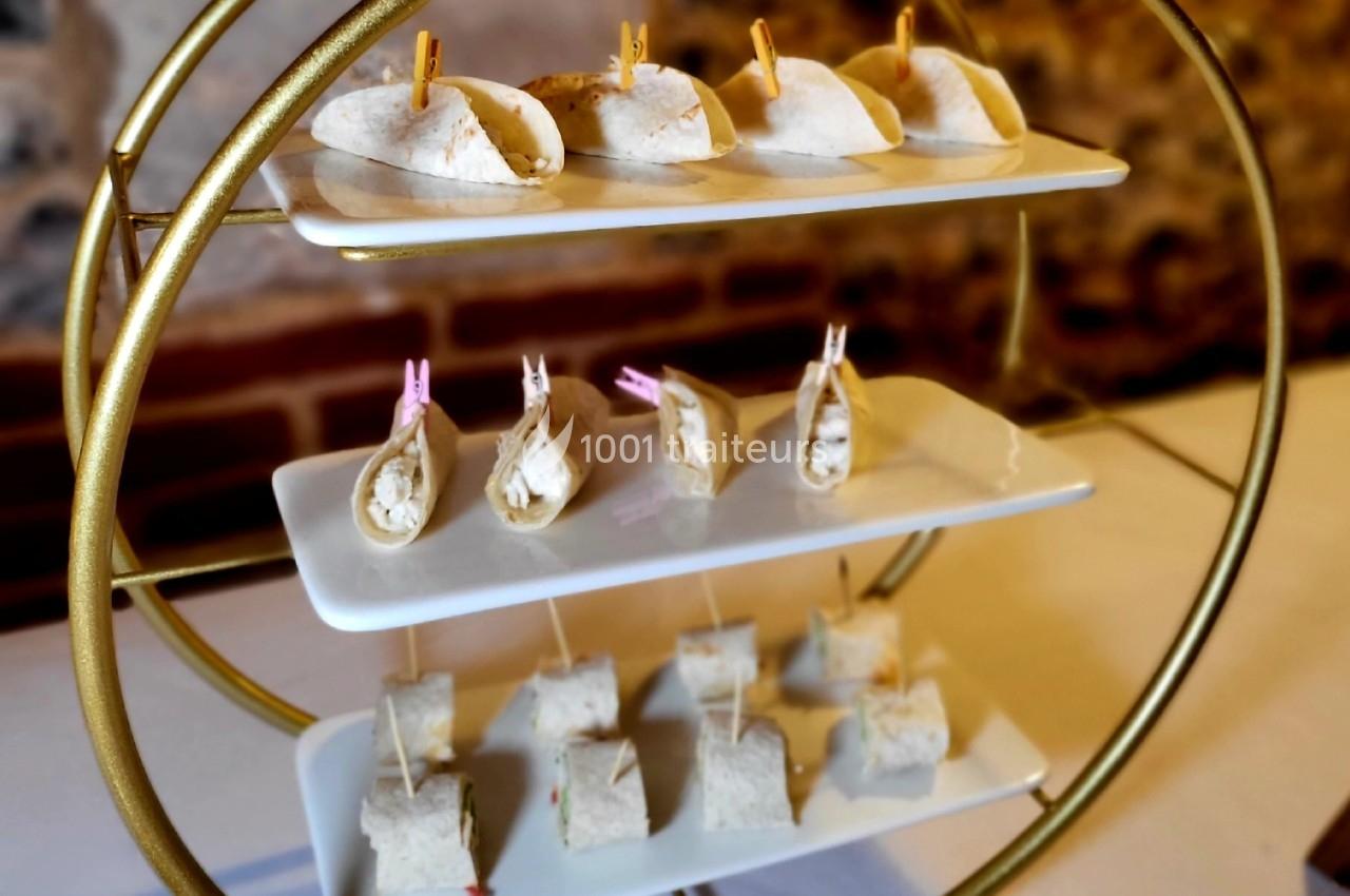 Présentoir doré avec trois étages de plateaux contenant des amuse-bouches en tortillas pliées et roulées.