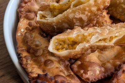 Une personne coupe un oignon sur une planche en bois, entourée de légumes frais et d'herbes aromatiques.