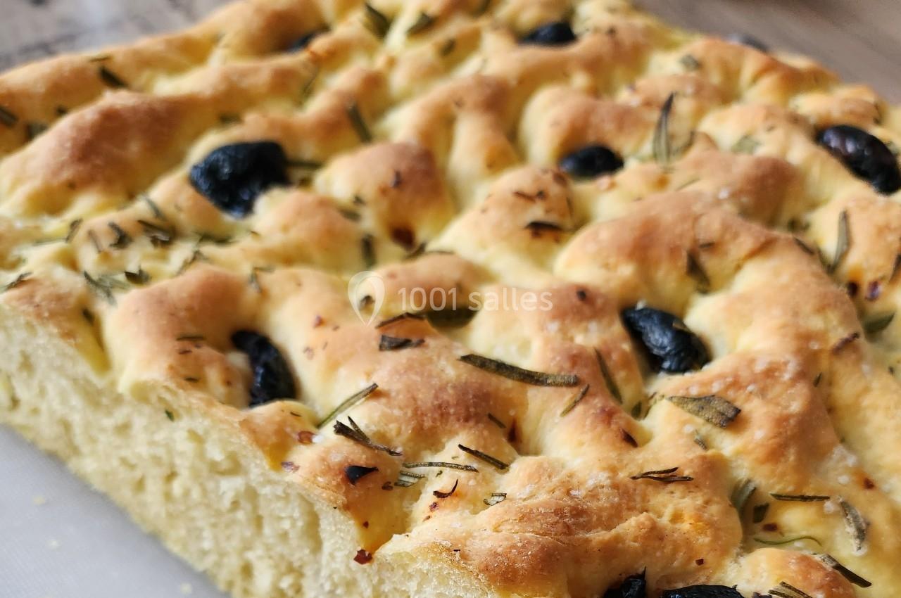 Focaccia dorée garnie d'olives noires et de brins de romarin sur une surface en bois.