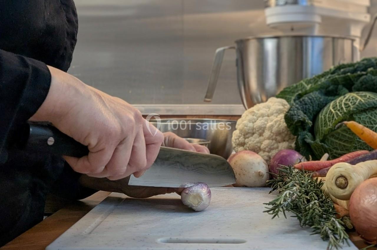 Une personne coupe un petit légume sur une planche, entourée de légumes frais et d'ustensiles de cuisine.