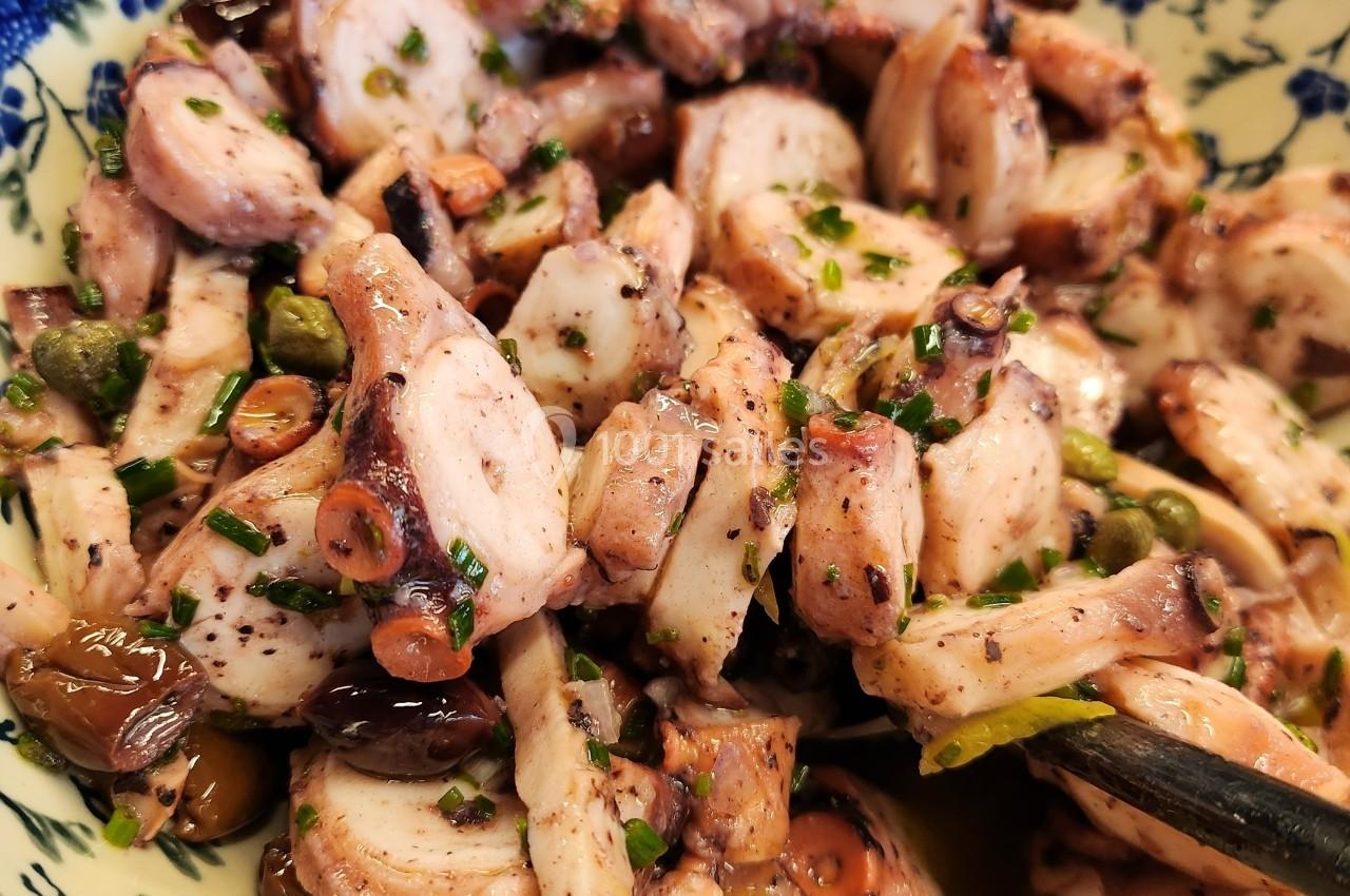 Salade de poulpe assaisonnée avec des herbes fraîches, servie dans un bol en céramique décoré de motifs bleus.