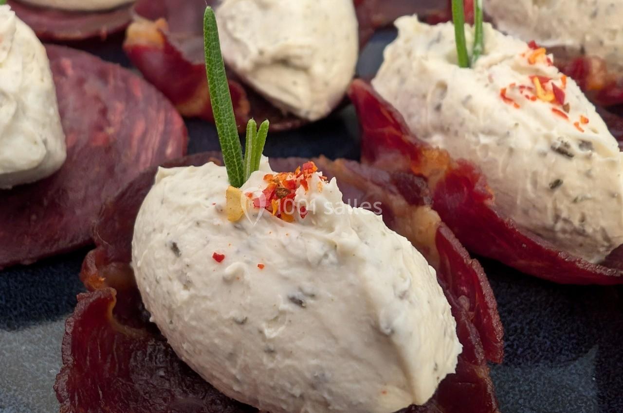 Tranches de viande séchée garnies de quenelles de fromage frais, décorées de brins de romarin et de piment.