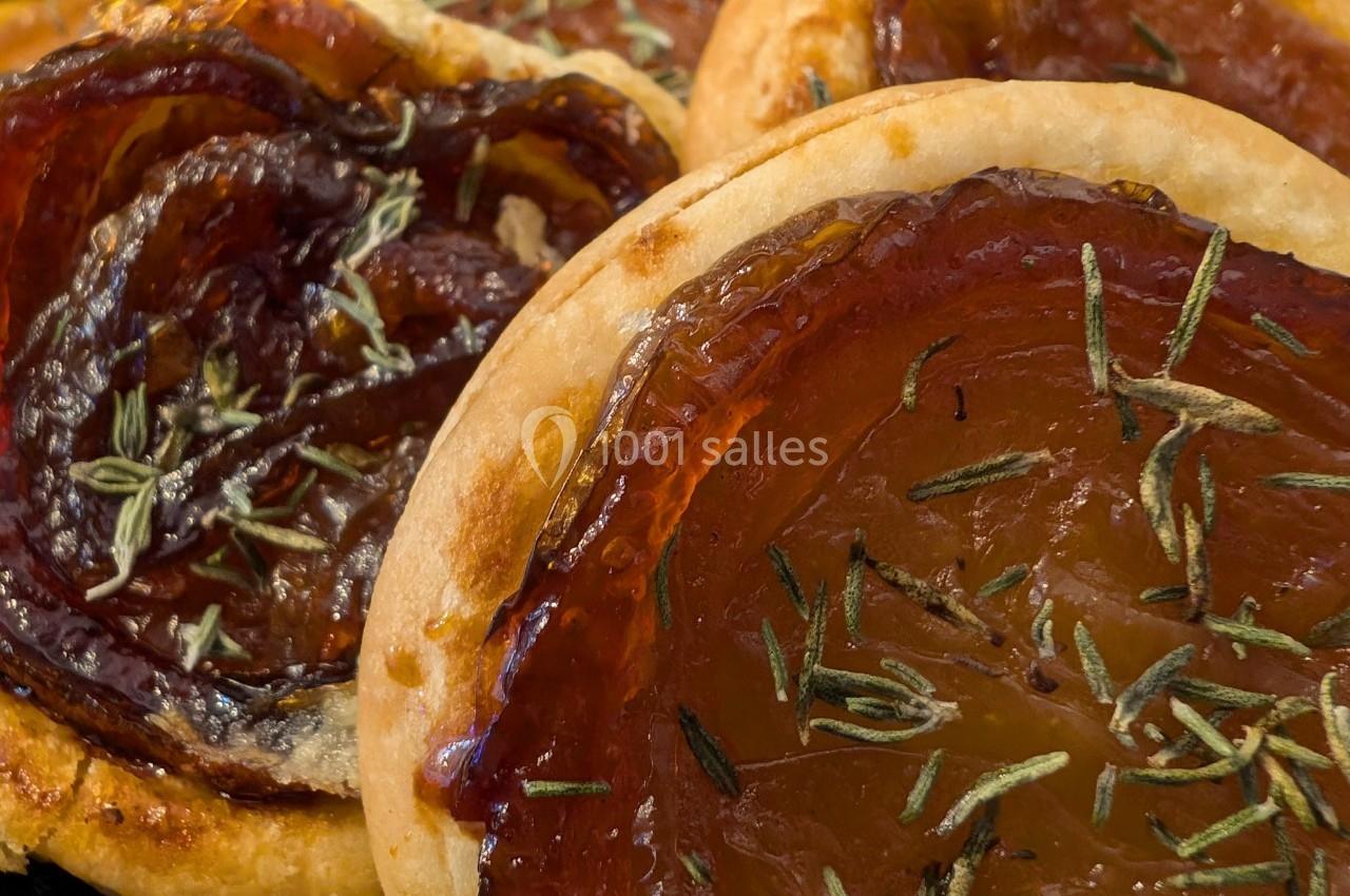 Tartelettes fines garnies de tranches de tomates caramélisées et saupoudrées d'herbes aromatiques, servies sur une assiette.