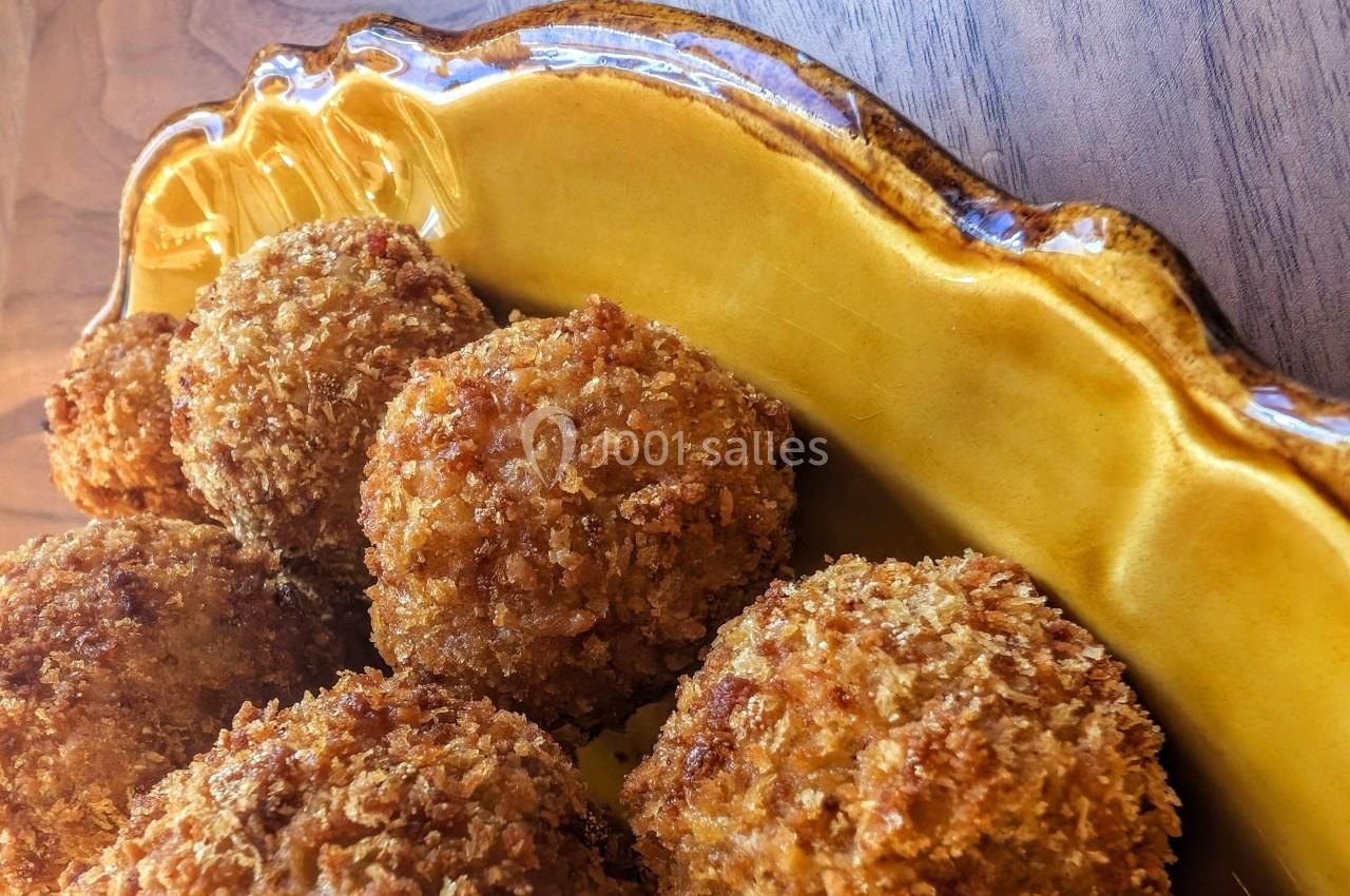 Boulettes panées dorées servies dans un plat en céramique jaune sur une table en bois.