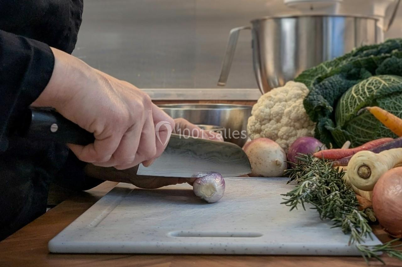Personne coupant un navet sur une planche à découper, entourée de légumes frais dans une cuisine.