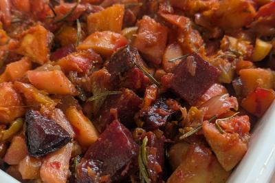 Une personne découpe un petit oignon sur une planche, entourée de légumes frais et d'herbes aromatiques.