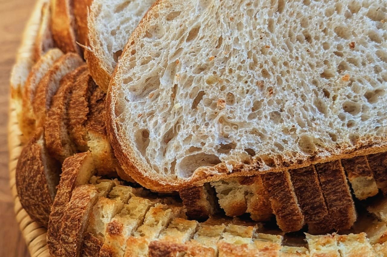 Tranches de pain artisanal disposées en éventail dans un panier en osier sur une table en bois.