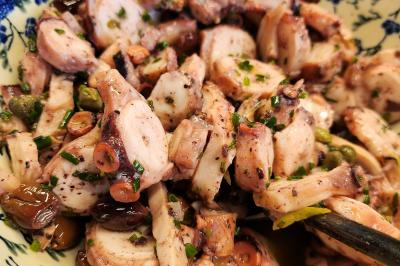 Une personne découpe un petit oignon sur une planche, entourée de légumes frais et d'herbes aromatiques.