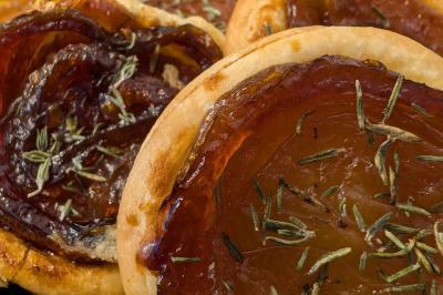 Une personne découpe un petit oignon sur une planche, entourée de légumes frais et d'herbes aromatiques.