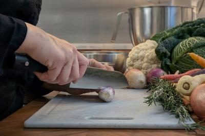 Une personne découpe un petit oignon sur une planche, entourée de légumes frais et d'herbes aromatiques.