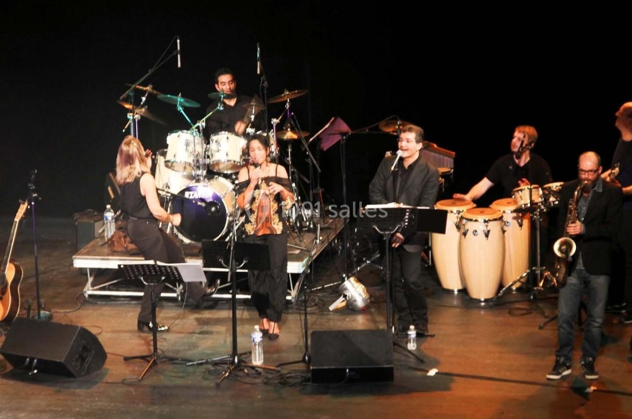 Un groupe de musiciens joue sur scène avec divers instruments, dont une batterie, des guitares et des percussions.