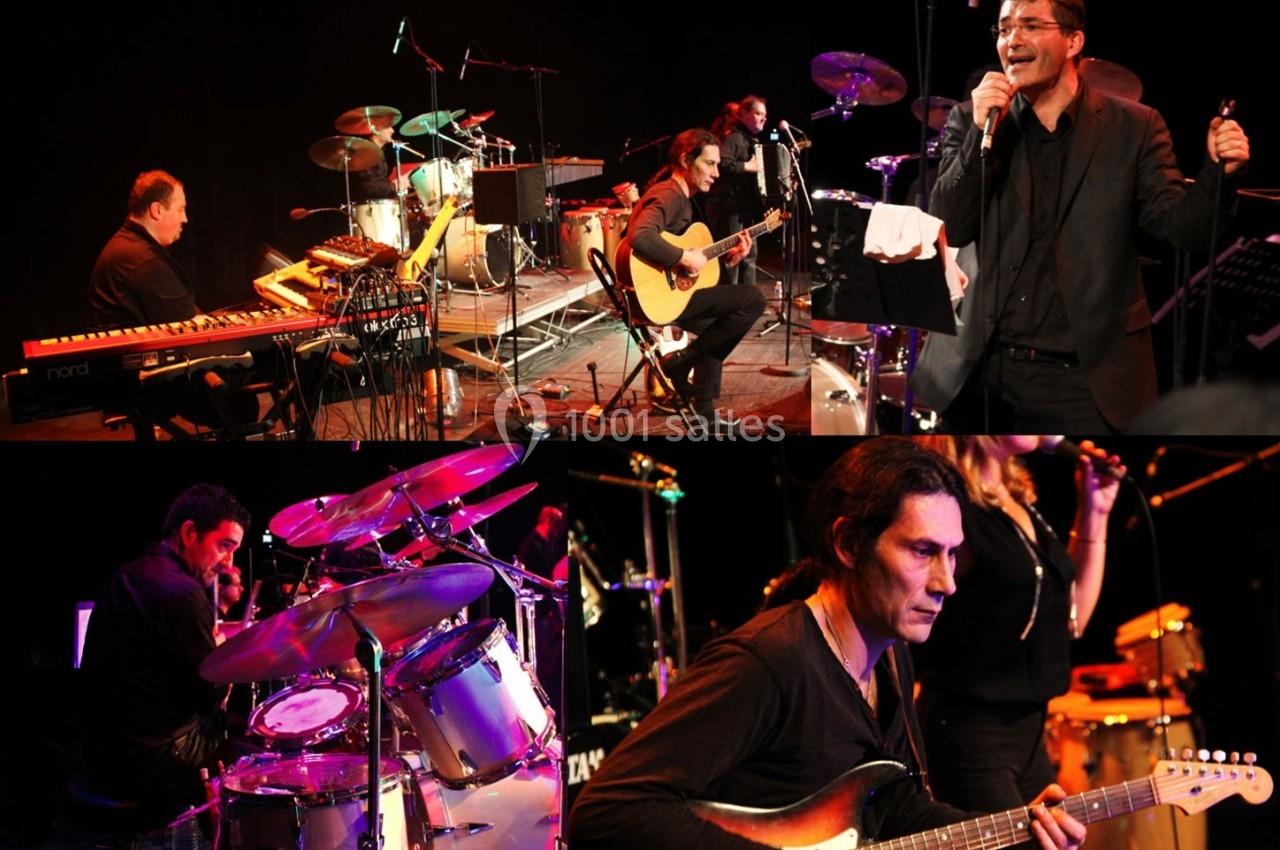 Musiciens jouant sur scène avec claviers, guitare, batterie et percussions, dans une ambiance de concert en direct.